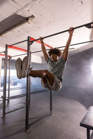 African American athlete performing hanging leg raises on pull-up bar in gym