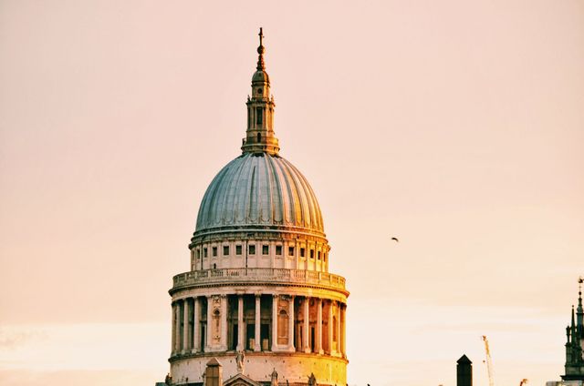 This image depicts the dome of a historical church building bathed in the warm hues of a setting sun. The structure's classic architectural details are highlighted, creating a serene atmosphere. Ideal for travel blogs, educational materials on architecture, or promotional content for tourism in London.