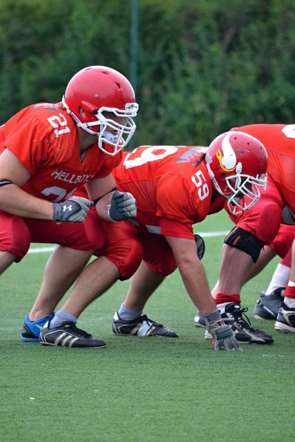 American football players in red uniforms playing while positioned on a field. Useful for depicting teamwork, sports competitions, athletic training, and outdoor activities. Excellent for sports-related advertisements, articles or blogs about football, and physical education resources.