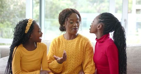 African American mother and daughters sharing warm conversation on sofa in bright room