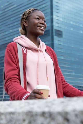 African american woman smiling while holding coffee cup at urban plaza with glass high-rise