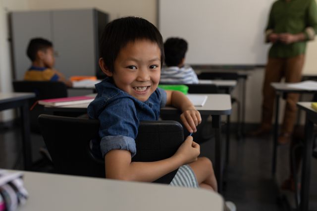 Young boy sitting in classroom, smiling and looking back. Can be used for educational content, school brochures, back-to-school campaigns, and promoting positivity in learning environments.