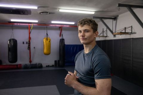 Young boxer standing in training gym clasping hands near heavy bags wearing dark tee