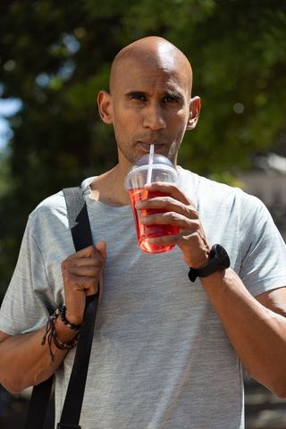 African american man drinking red beverage outdoors holding strap, urban summer portrait