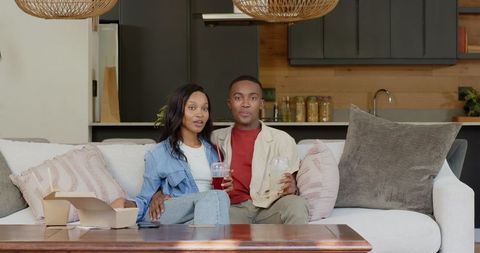 Relaxed African American Couple Enjoying Drinks on Comfortable Sofa