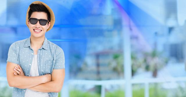 Man wearing sunglasses and hat standing with arms crossed, smiling freely against a modern urban backdrop. Ideal for travel, tourism promotions, casual lifestyle ads, fashion blogs, and summer-themed content.