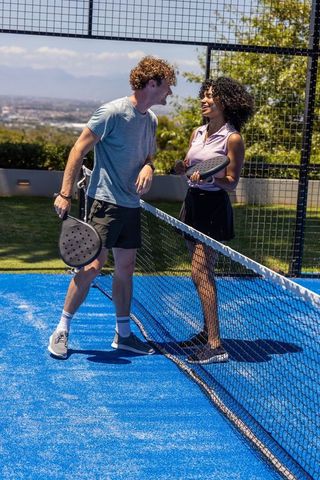Smiling diverse couple playing pickleball at net on vibrant blue court with city views