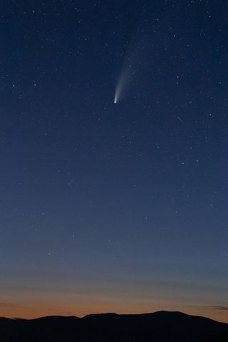 Comet streak and starry sky over dusk landscape
