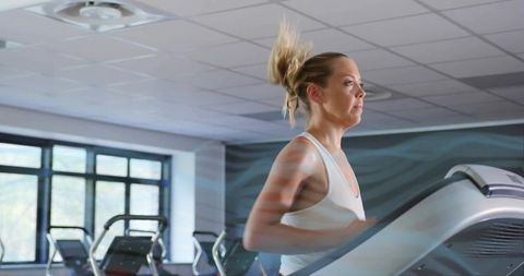 Woman Running on Treadmill in Modern Gym with Sunlit Windows