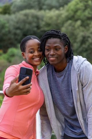 African american couple taking selfie outdoors by park railing smiling in casual activewear