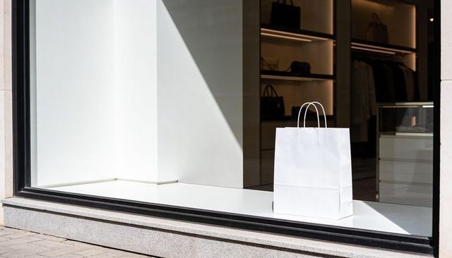 White paper bag displaying minimalist boutique window with dramatic sun shadow
