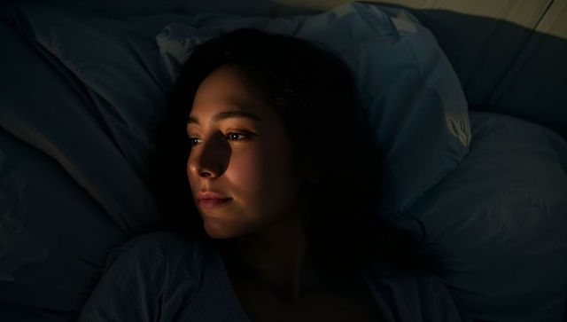 Woman resting in bed under warm light at night moody chiaroscuro dramatic shadows