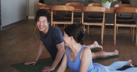 Couple practicing yoga at home smiling while stretching on mats in dining room
