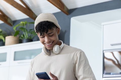 Smiling african american man checking smartphone in modern kitchen wearing headphones