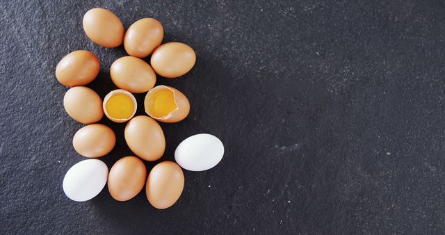 Brown and white eggs are arranged on a dark surface, one cracked open to reveal a bright yellow yolk. Eggs are a versatile ingredient, essential in many recipes and a symbol of new beginnings.