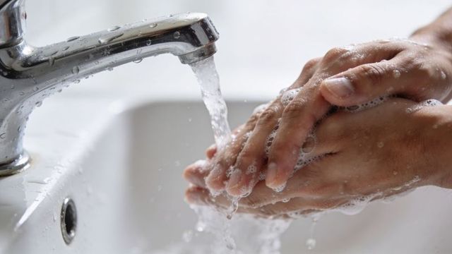 Washing hands under running faucet with soapy lather for hand hygiene and germ prevention
