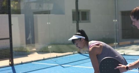 Leaning player holding paddle recovering from rally on blue outdoor paddle tennis court