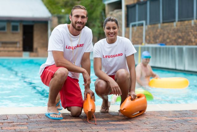 Portrait of male and female lifeguards holding rescue cans at poolside