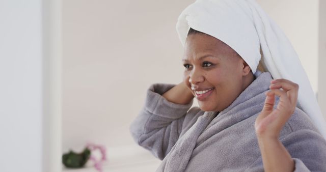 African American woman wearing bathrobe and towel on head after shower is smiling. Perfect for content about self-care routines, spa treatments, relaxation at home, or personal hygiene