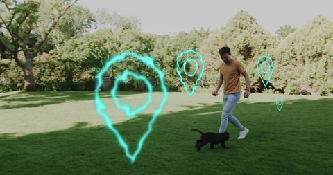 Young man walking and playing with black puppy in park with glowing location pins