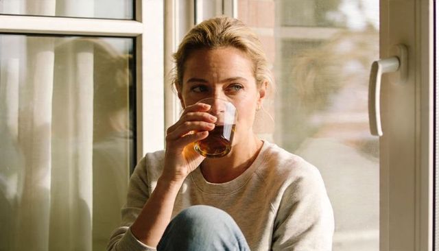 Contemplative woman sipping warm beverage by window in casual sweatshirt morning light