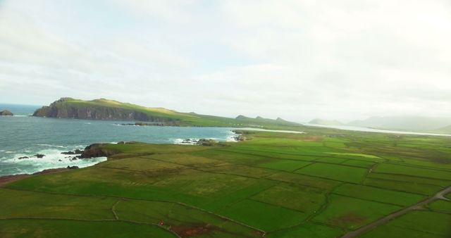 Aerial view captures the scenic beauty of lush green coastal farmland and striking cliffs along the ocean. Ideal for travel blogs, nature documentaries, and promotional material for outdoor destinations.