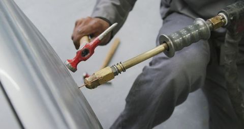 African american mechanic repairing car fender with slide hammer for dent removal