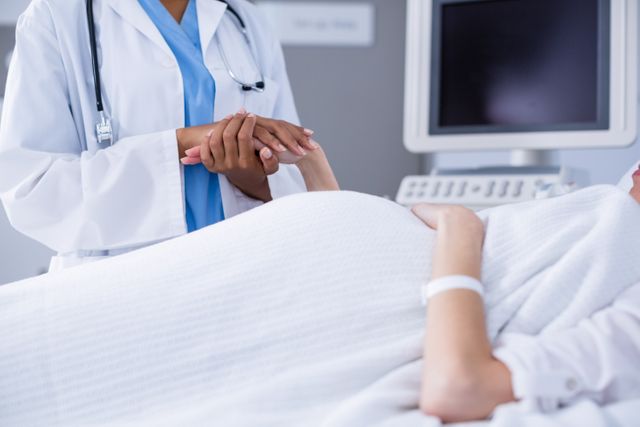 Doctor holding hand of pregnant woman during ultrasound scan in hospital. Useful for topics on prenatal care, medical support, healthcare services, and maternity. Ideal for medical websites, healthcare brochures, and pregnancy-related articles.