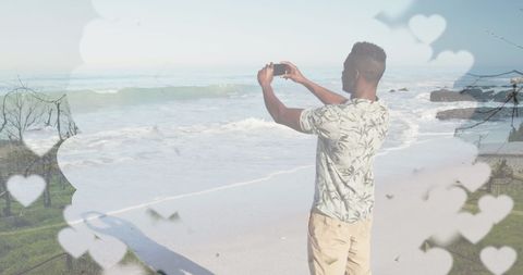 Man Taking Photo of Beach Views with Smartphone Amid Heart Frames