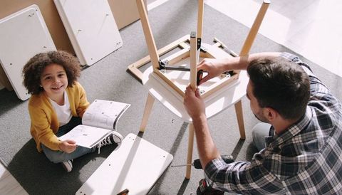Father assembling wooden chair while child reading manual and smiling at home