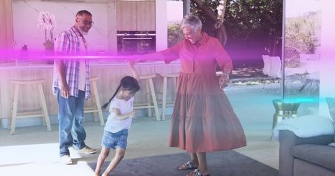 Grandmother guiding granddaughter twirling in modern open-plan kitchen, grandparent bonding