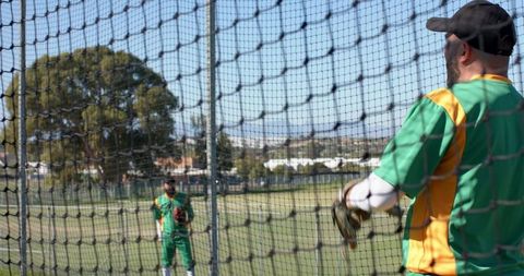 Male cricket teammates practicing in batting net wearing green yellow kits and gloves