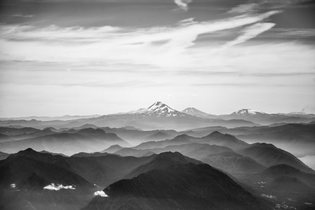 Black and white panoramic view of a misty mountain range with clouds drifting above. Suitable for use in travel brochures, nature photography collections, backgrounds for presentations, and inspirational posters.