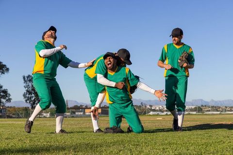 Diverse Baseball Team Celebrating Victory on Field, Kneeling and Hugging in Green Uniforms