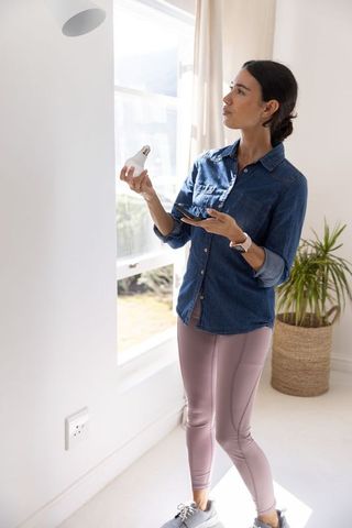 Woman installing led bulb in bright living room using smartphone for smart lighting