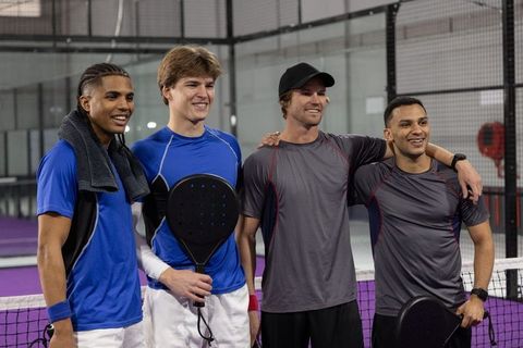 Four male players posing shoulder-to-shoulder on indoor paddle court after doubles match
