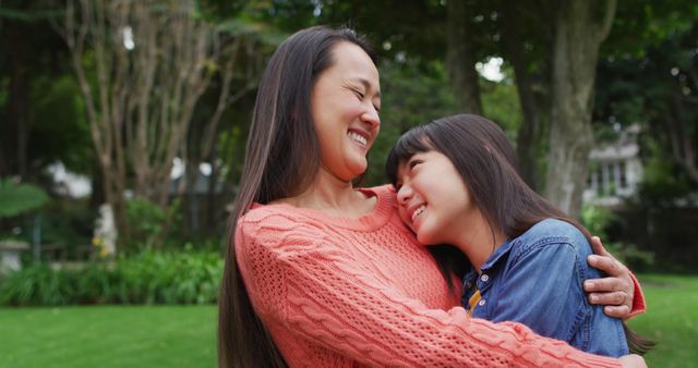 Mother and daughter sharing a happy moment and hugging in a park with trees and greenery in the background. Perfect for use in family, parenting, and happiness themes. Ideal for advertisements or articles focusing on family bonds and outdoor activities.