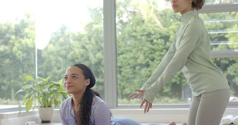 African American Instructor Guiding Student Through Gentle Mat Stretches in Sunlit Studio
