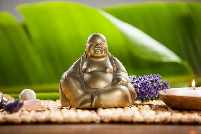 Laughing buddha figurine, lit candle and pebbles stone on mat