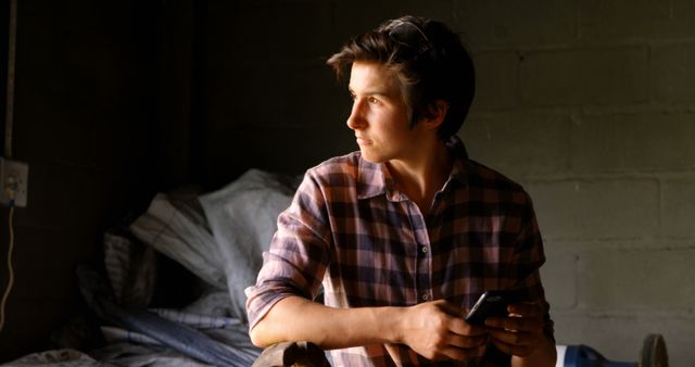 Young Man Holding Smartphone Looking Thoughtful in Dimly Lit Room - Download Free Stock Images Pikwizard.com