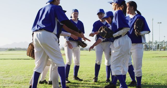 Group of young baseball players standing in a circle engaging in a team huddle before their game. They are wearing matching blue and white uniforms, gloves and caps. This photo represents teamwork, motivation, and sportsmanship, making it ideal for use in sporting event promotions, youth sports league advertisements, educational materials about teamwork, and articles focusing on the benefits of youth participation in sports.