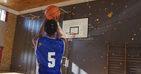 Shooting basketball player in blue jersey number 5 practicing jump shot in school gym with confetti