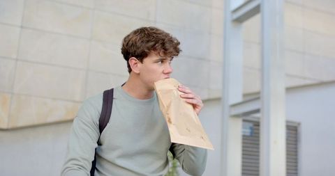 Young commuter breathing into paper bag outside modern urban building