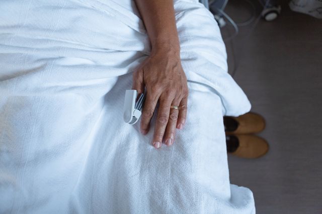 Image shows a male patient lying in a hospital bed with a pulse oximeter on his finger, indicating he is receiving medical treatment. This image can be used for healthcare, medical treatment, patient care, and hospital-related content.