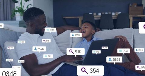 Father and son relaxing on sofa sharing laptop with social media notification badges