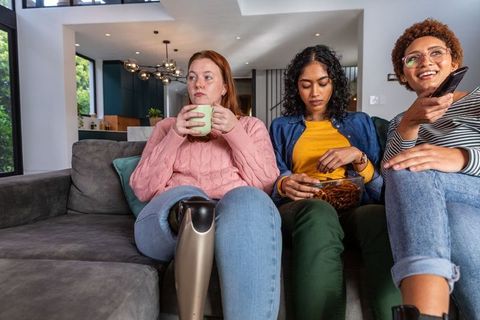 Diverse Women Relaxing on Sofa at Home with Snacks and Remote