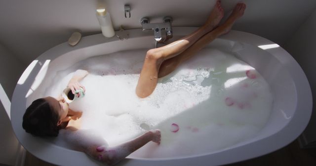 Woman soaking in bubble bath, sipping coffee. Ideal for articles on self-care, relaxation techniques, home spa, wellness tips, or lifestyle imagery.