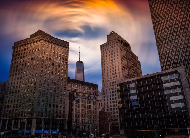 Surreal downtown scene featuring a majestic skyline with tall skyscrapers and buildings under a dramatic swirling cloud formation at sunset. The vibrant colors of the sky create a unique and artistic ambiance. Ideal for use in urban themed projects, architectural exhibitions, and creative backgrounds for design and digital art.