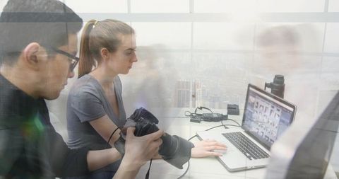 Photographer and editor collaborating over dslr and laptop with urban skyline, reflections