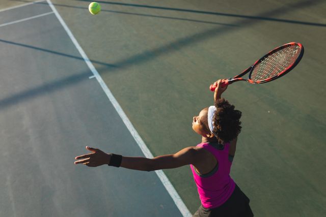 High angle view of african american young female player serving at tennis court on sunny day. unaltered, sport, competition and tennis game concept.